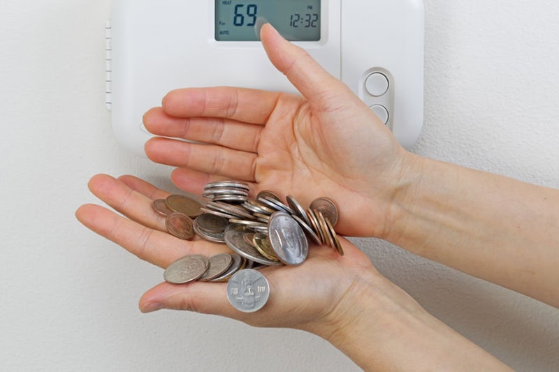 hands holding coins in front of a thermostat.