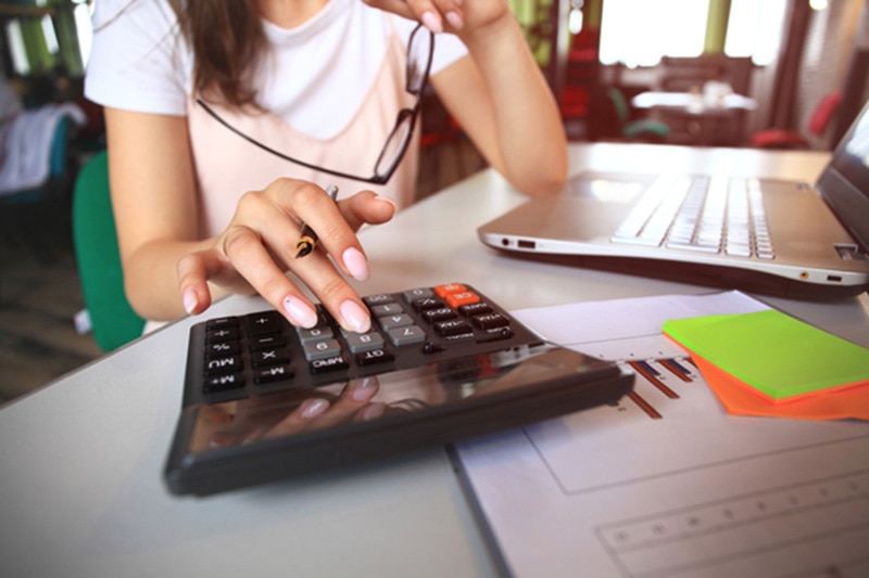 Young woman at desk typing on a calculator, How Do I Finance My New Air Conditioning System? | HVAC Purchasing