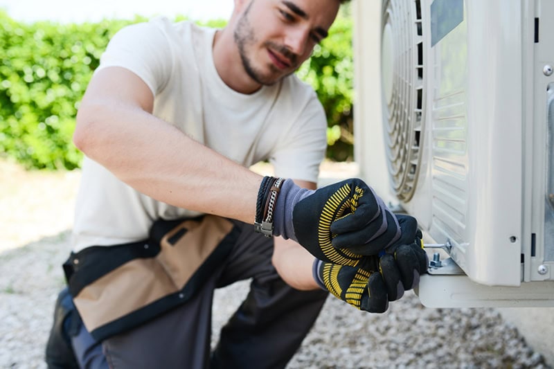 Young man electrician repairing air conditioning in client house, Repair or Replace Your AC? 5 Factors to Help | HVAC Service