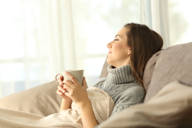 Portrait of a pensive woman relaxing sitting on a sofa in the living room in a house interior in winter