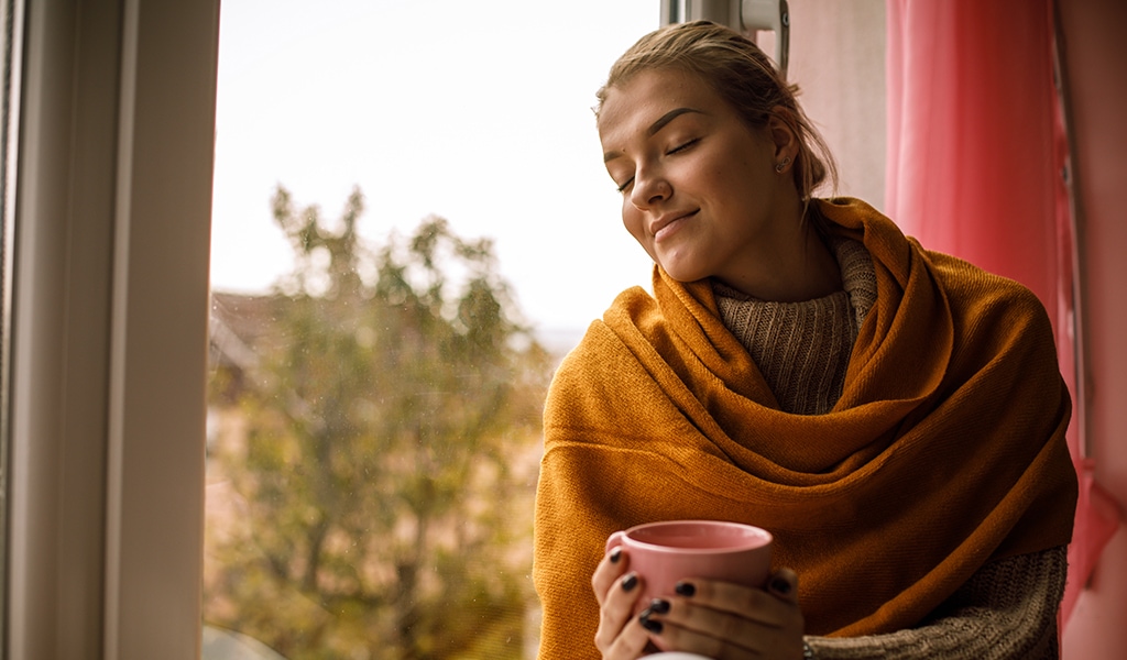 Smiling young woman enjoying a warm cup of tea on a cold autumn day