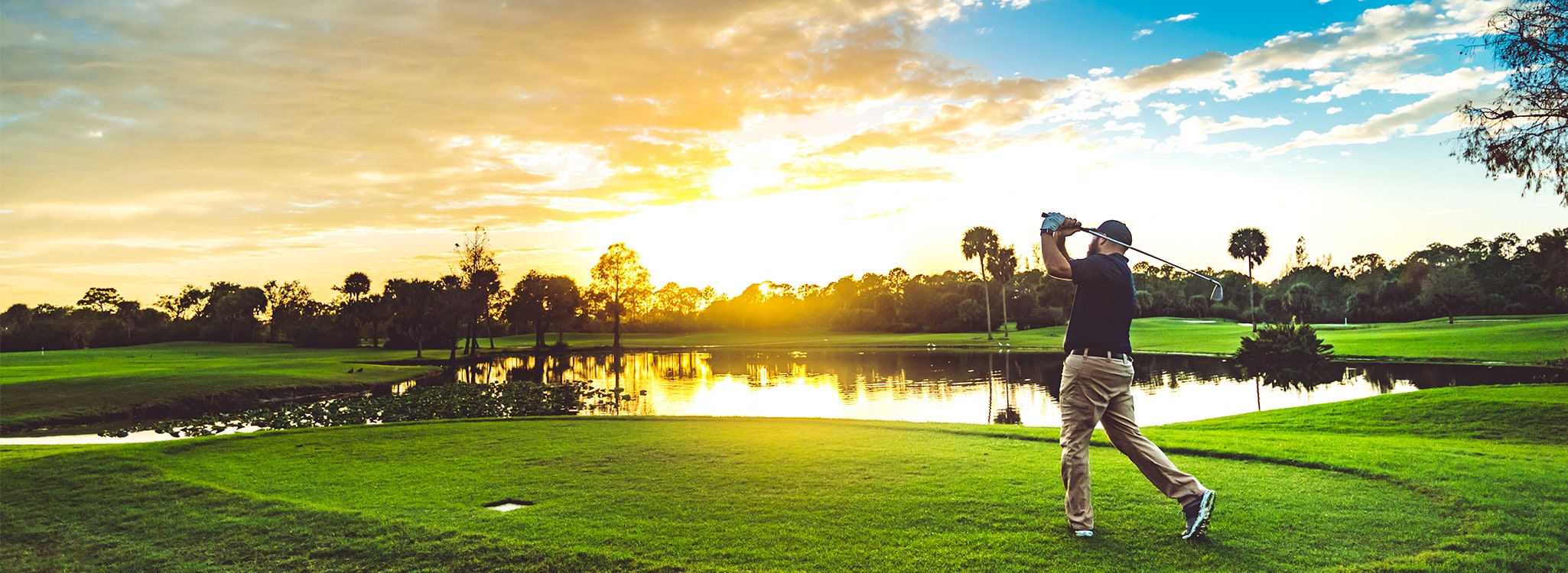 Golfer swinging a club at a course at sunset.