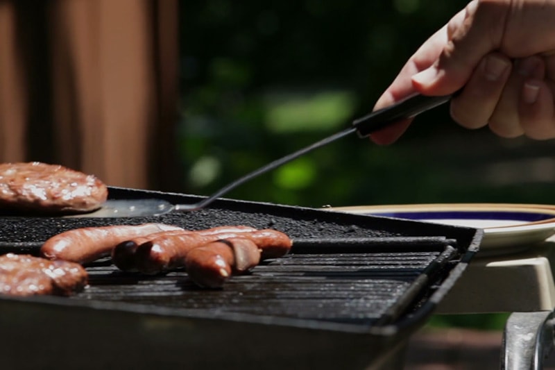 someone cooking hotdogs on their grill to save energy