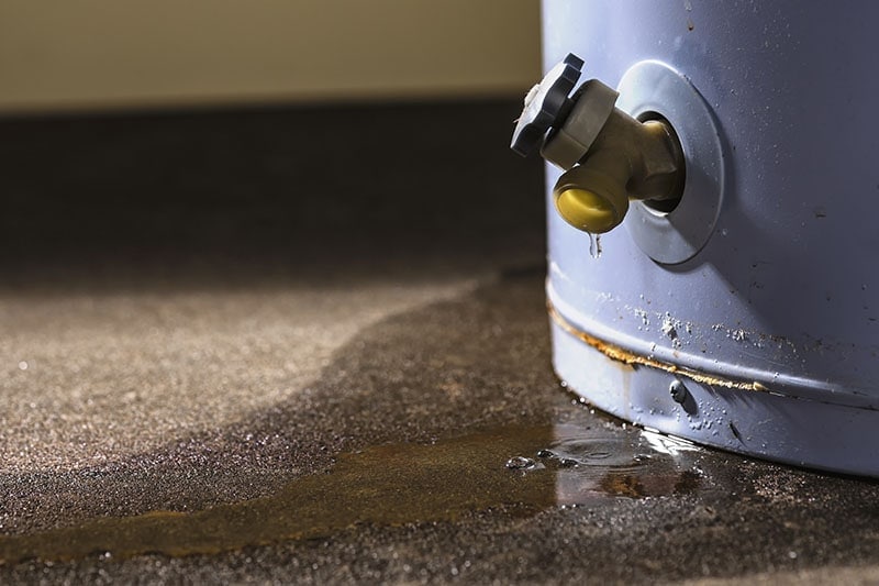 Water leaking from the plastic faucet on a residential electric water heater sitting on a concrete floor. Water Heater Problems