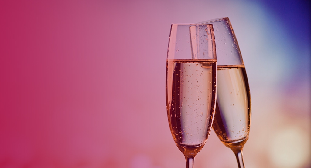 two mostly full champagne glasses ready against a blurred background and pink overlay.